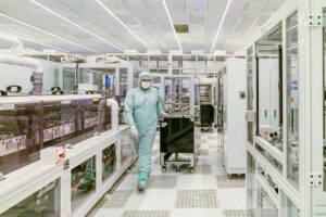Scientist in protective gear walking in a high-tech cleanroom laboratory environment.